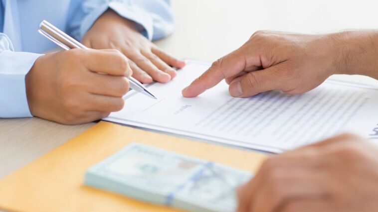 one person is holding loan tenure documents and money, while the other is signing it